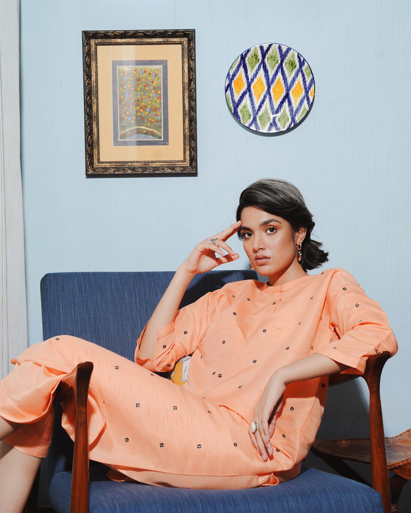 Model in a peach embroidered suit seated in a blue armchair