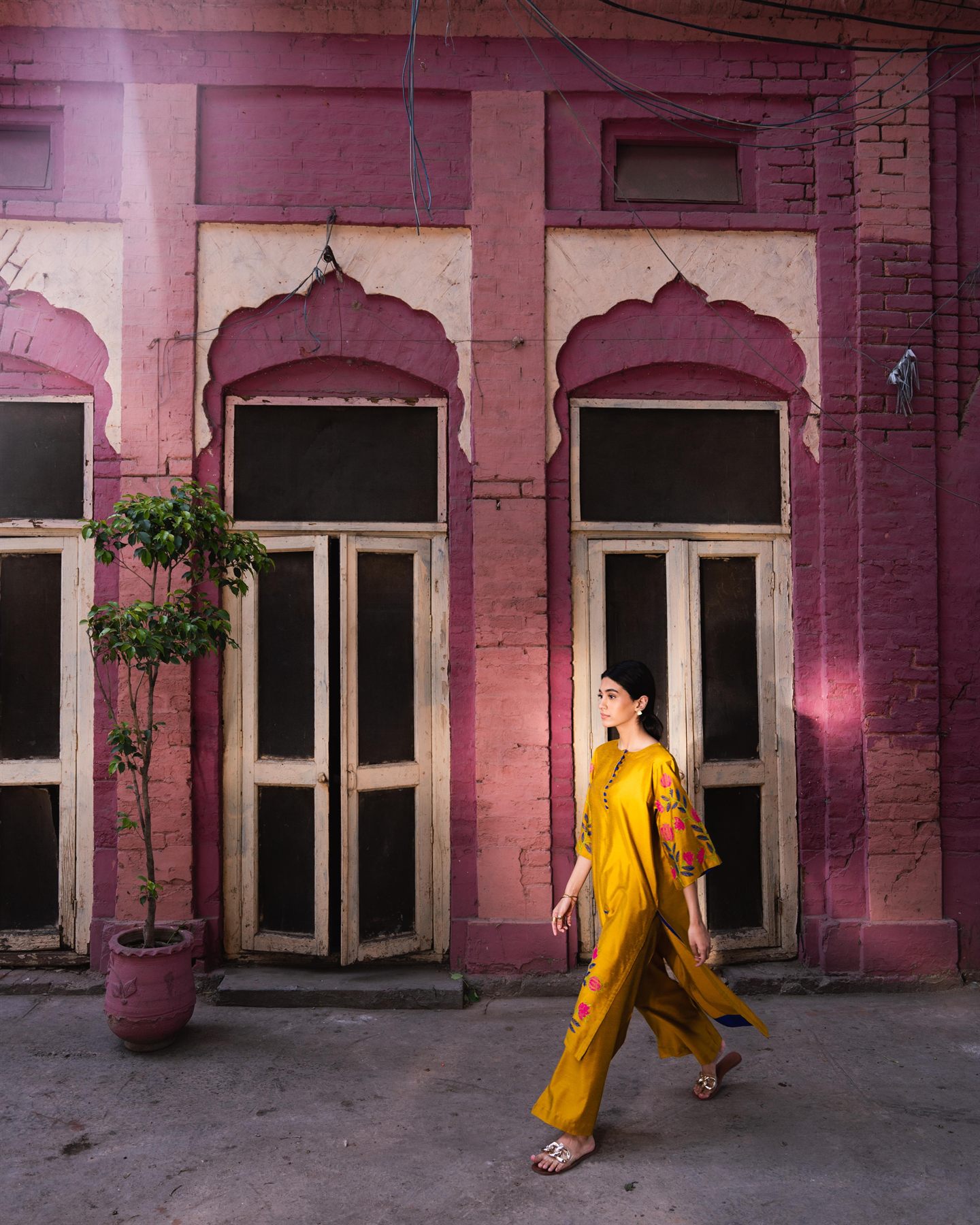 Model in yellow walking past a pink haveli facade