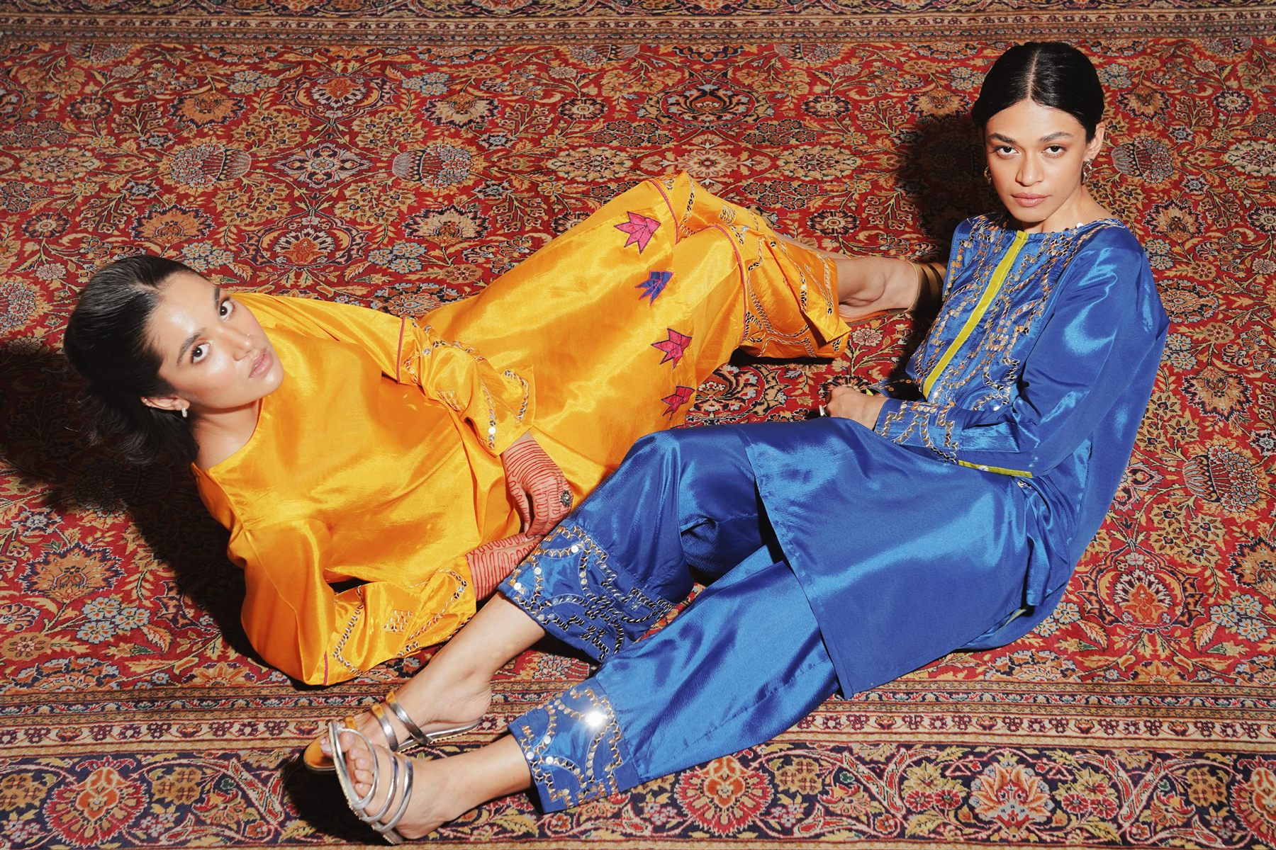 Two models in ochre and cobalt silk reclining on a Persian rug