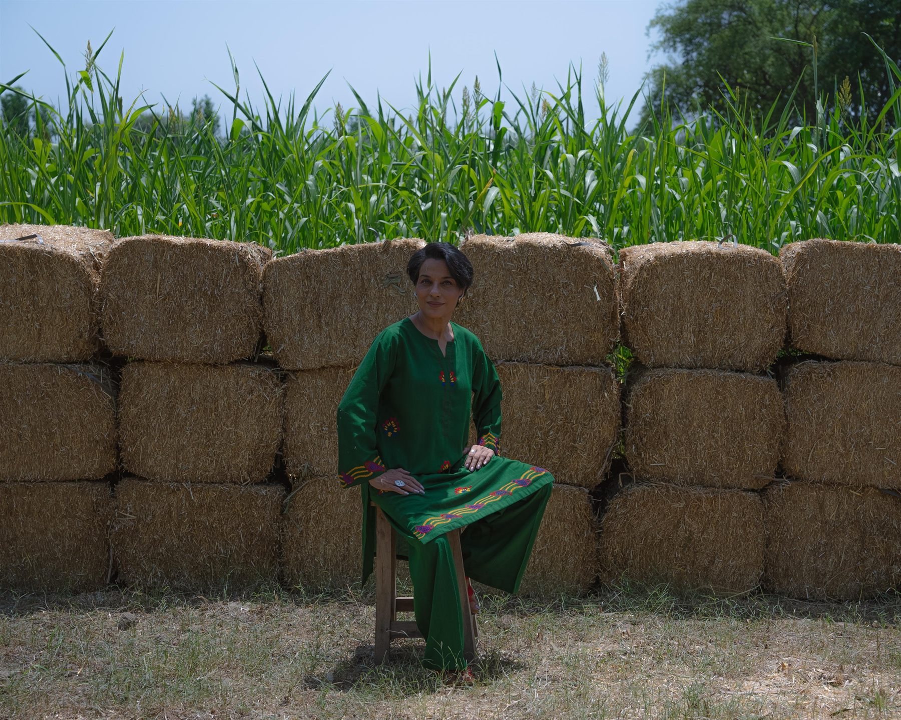 Model in green seated before hay bales and a cornfield