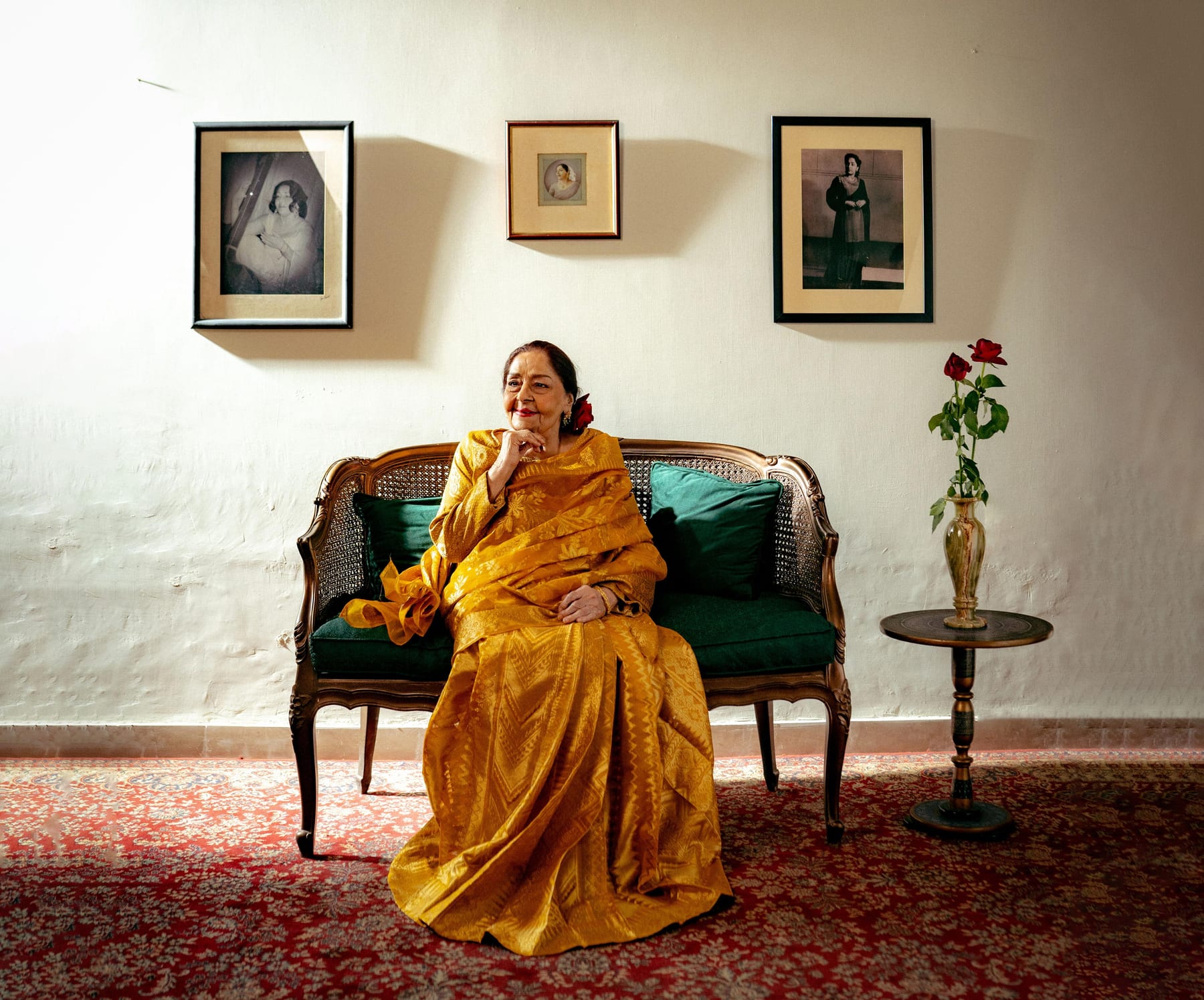 Farida Khanum in a mustard silk sari seated on a cane settee beneath framed portraits